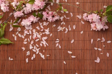 Photo of Beautiful blossoming branch and flower petals on bamboo mat, flat lay