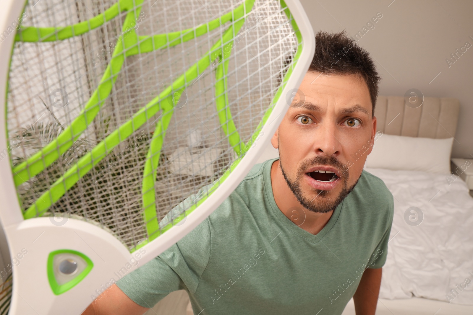 Photo of Man with electric fly swatter in bedroom. Insect killer