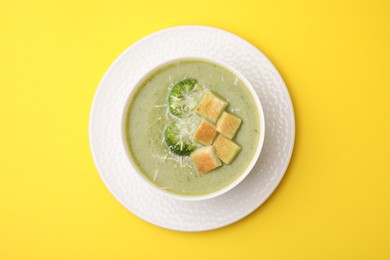 Photo of Delicious broccoli cream soup with croutons and cheese on yellow background, top view