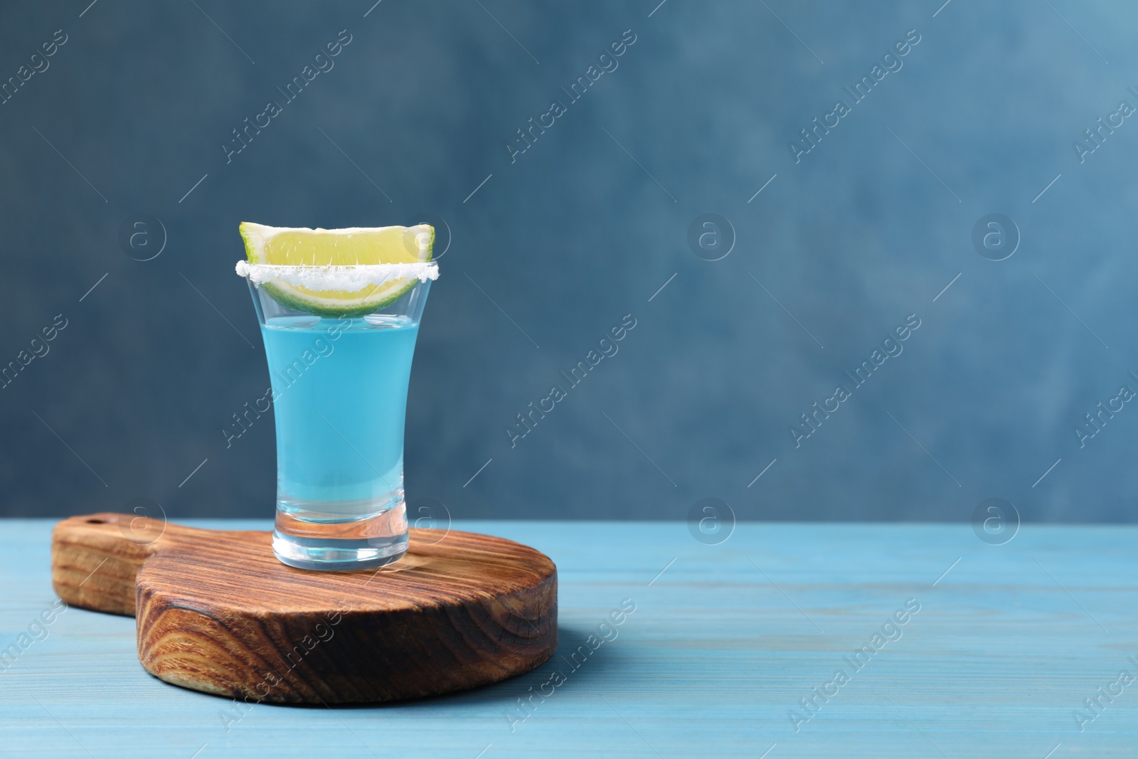 Photo of Light blue shot with lime on wooden table, space for text