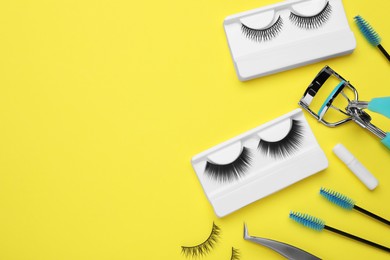 Flat lay composition with fake eyelashes, brushes and tools on yellow background. Space for text