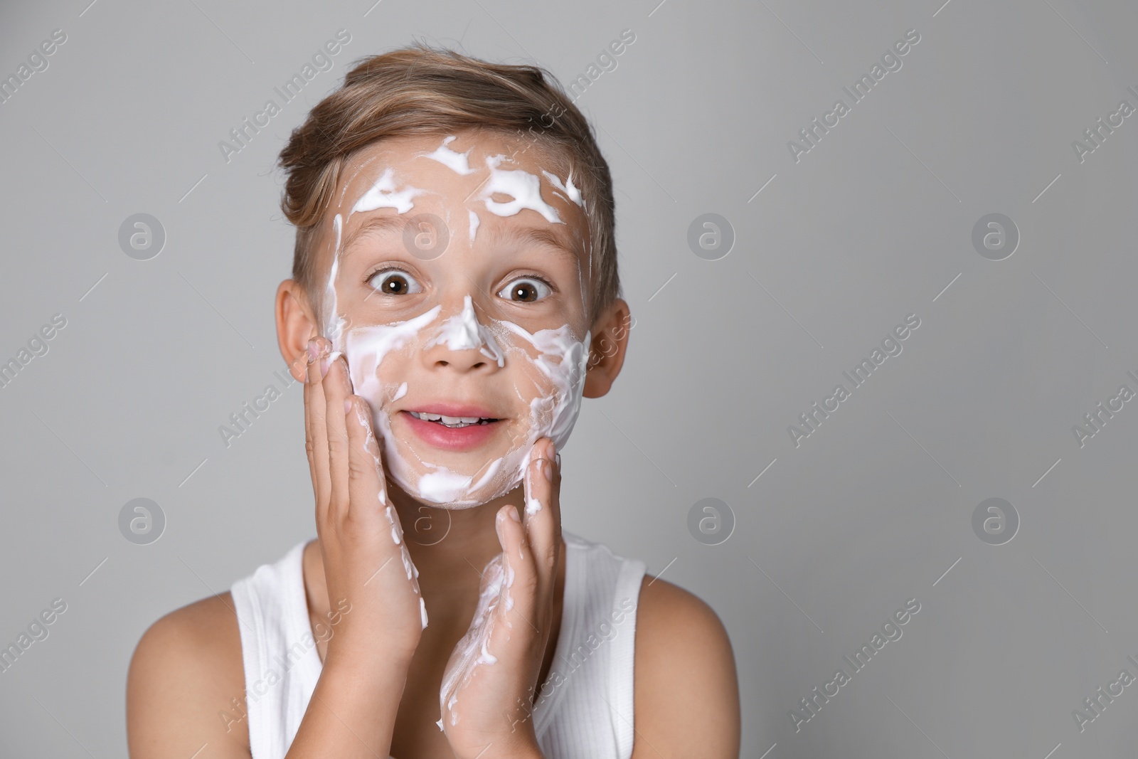 Photo of Cute little boy with soap foam on face against gray background