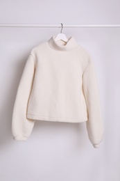 Warm sweater hanging on rack against white background