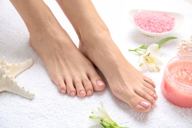 Photo of Woman with smooth feet, cosmetic and flowers on white towel, closeup. Spa treatment