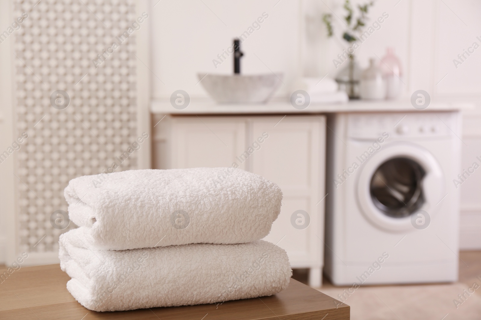 Photo of Clean folded towels on wooden table in laundry room. Space for text