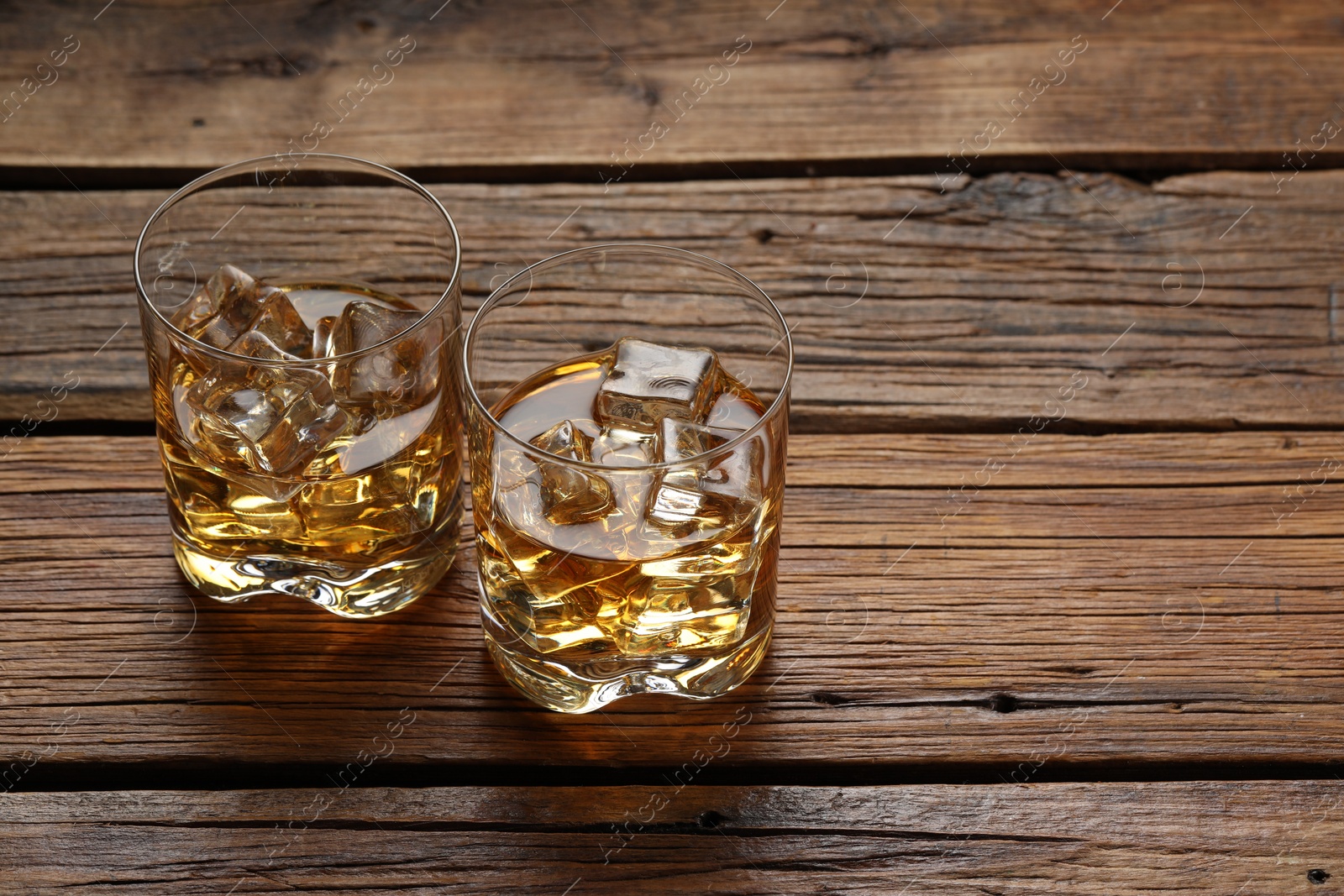 Photo of Whiskey with ice cubes in glasses on wooden table, space for text