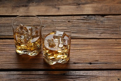 Photo of Whiskey with ice cubes in glasses on wooden table, space for text