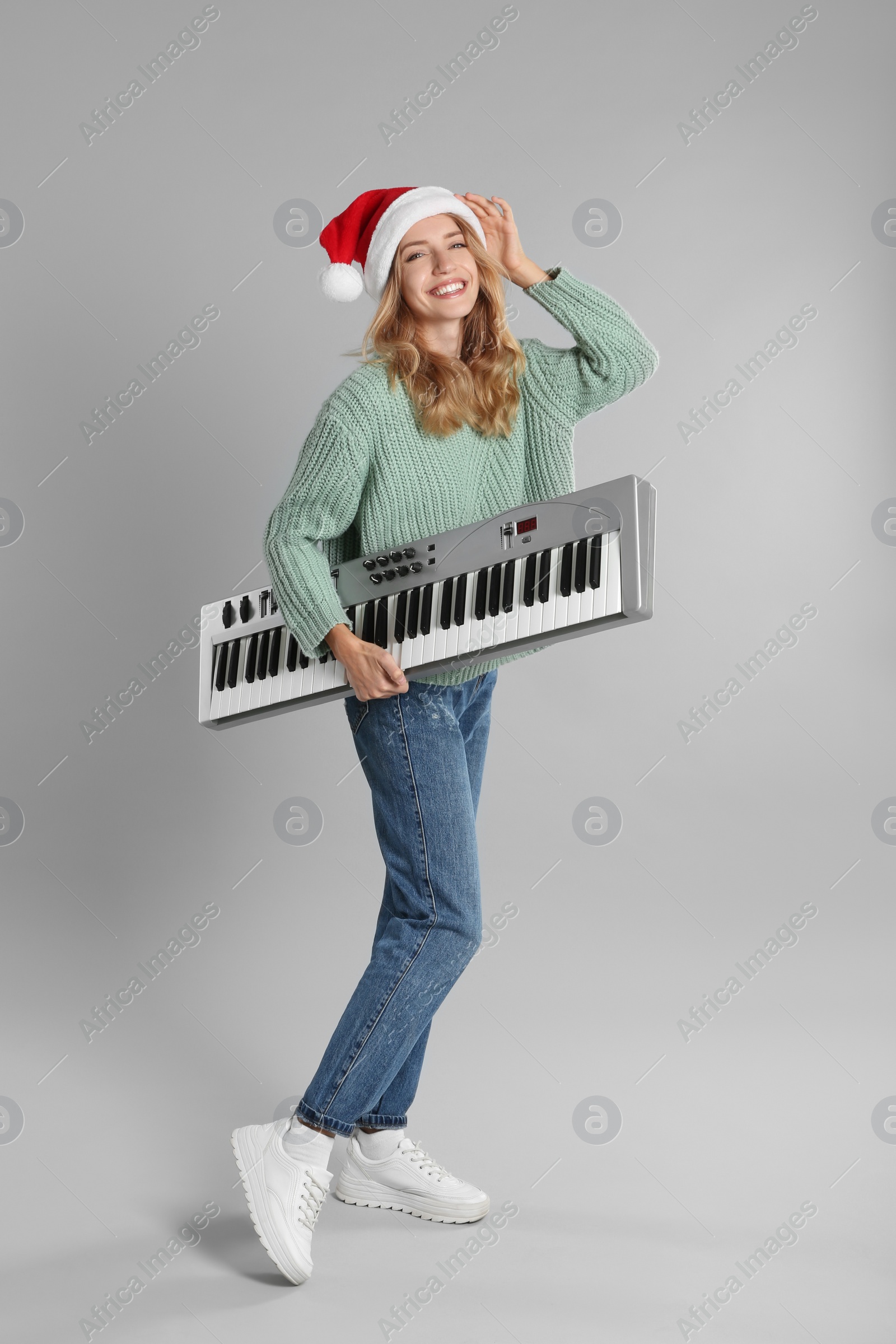 Photo of Young woman in Santa hat with synthesizer on light grey background. Christmas music