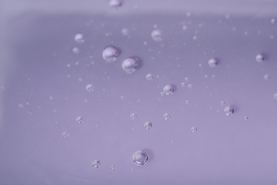 Photo of Pure transparent cosmetic gel on lilac background, closeup