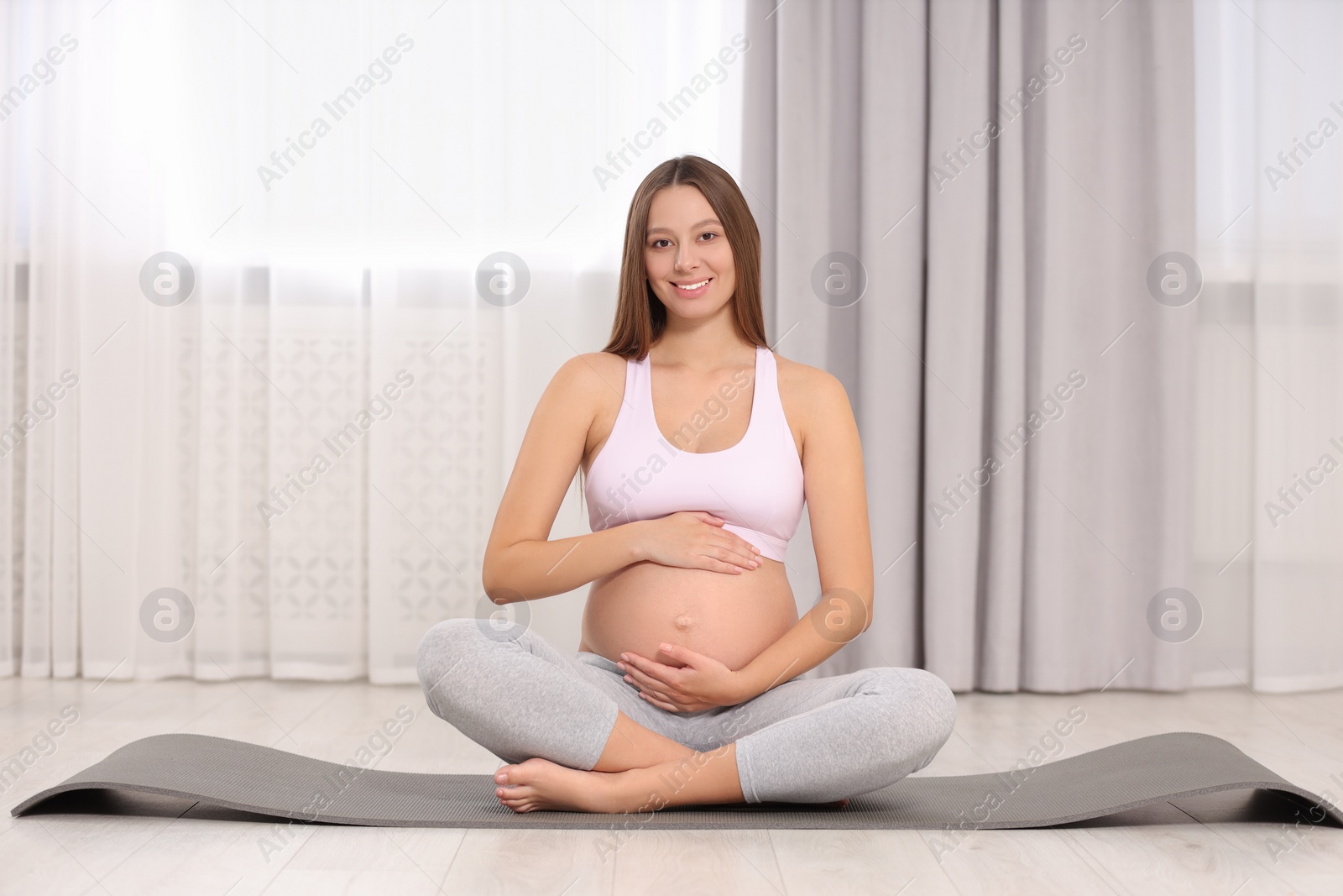 Photo of Pregnant woman sitting on yoga mat at home