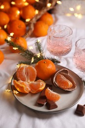 Delicious ripe tangerines, chocolates, festive lights and glasses of wine on white bedsheet