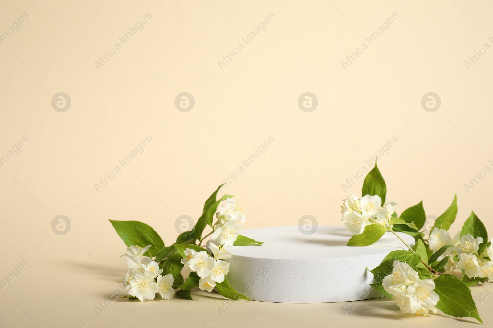 Photo of Presentation of product. White podium and beautiful jasmine flowers on beige background, space for text