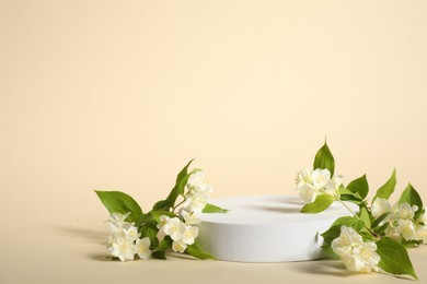 Presentation of product. White podium and beautiful jasmine flowers on beige background, space for text