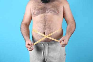 Photo of Fat man with measuring tape on color background, closeup. Weight loss