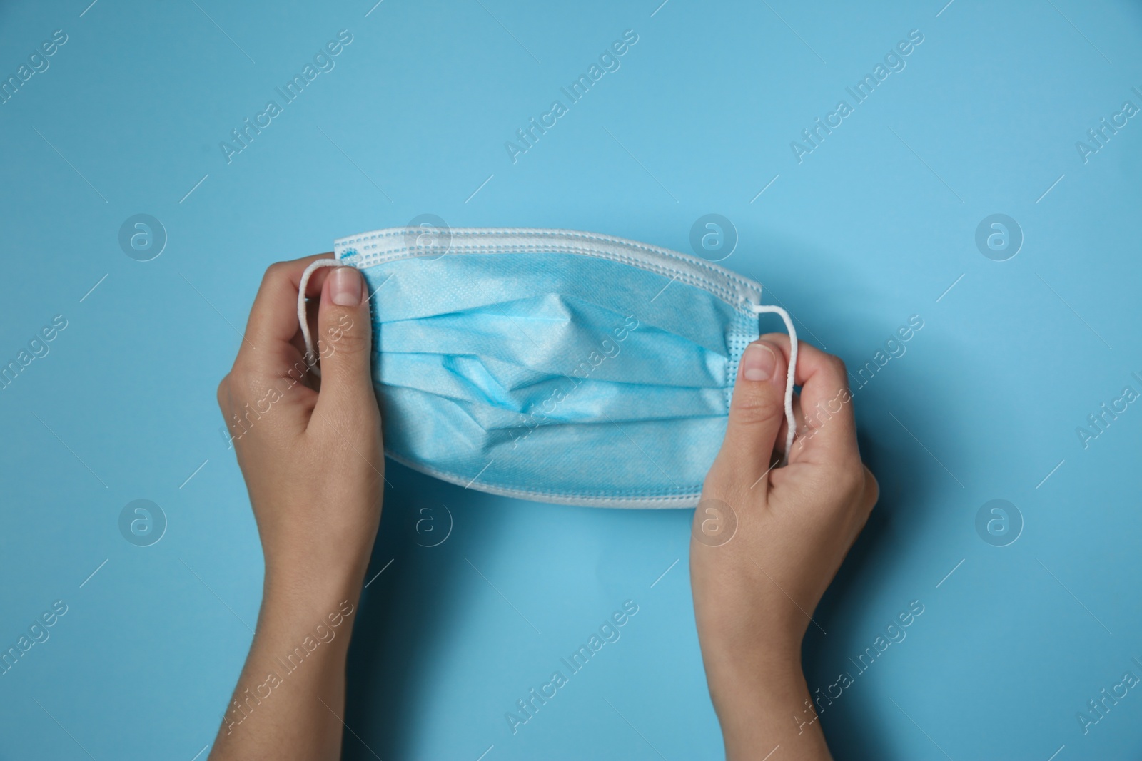 Photo of Woman holding disposable face mask on light blue background, closeup. Protective measures during coronavirus quarantine