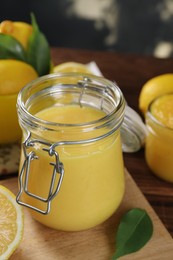 Photo of Delicious lemon curd in glass jar, fresh citrus fruit and green leaf on table