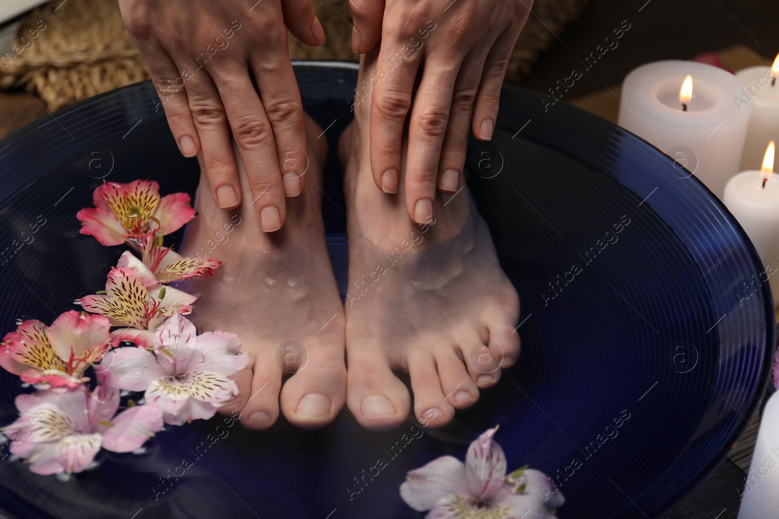 Photo of Woman soaking her feet in bowl with water and flowers, closeup. Spa treatment