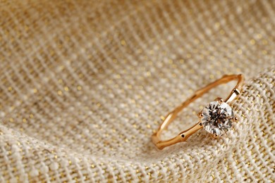 Photo of Beautiful engagement ring on sack fabric, closeup. Space for text