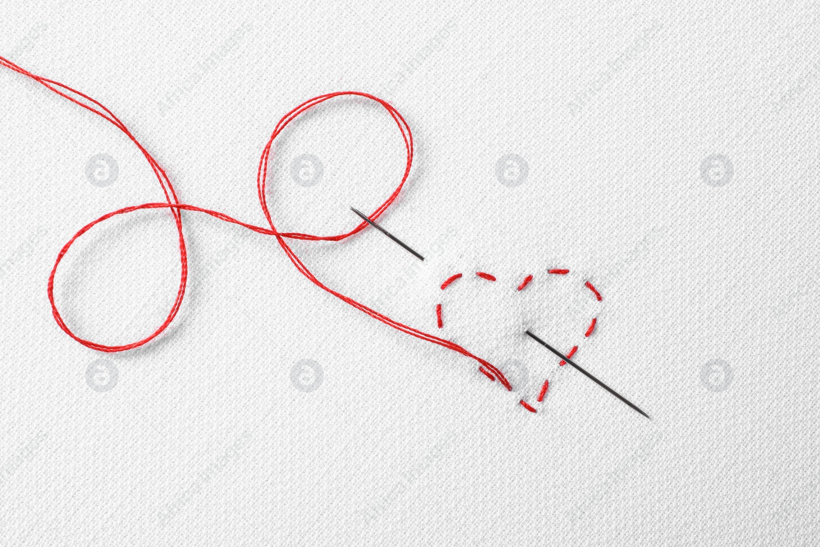 Photo of Needle with red thread and stitches in shape of heart on white fabric, top view