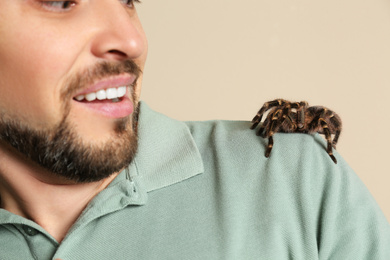 Photo of Scared man with tarantula on beige background, closeup. Arachnophobia (fear of spiders)