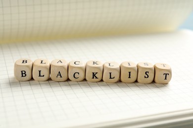 Photo of Wooden cubes with word Blacklist on notebook, closeup