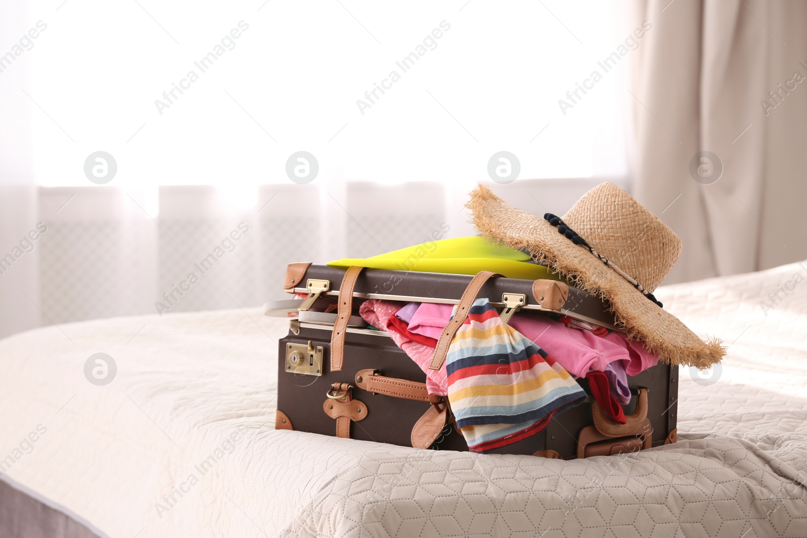 Photo of Vintage suitcase full of clothes on bed indoors. Space for text