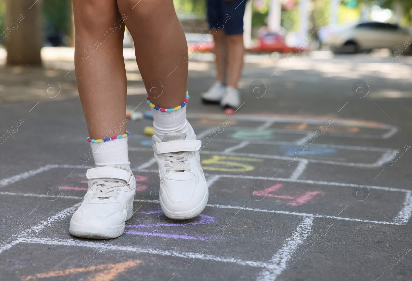 Photo of Little children playing hopscotch drawn with chalk on asphalt outdoors, closeup