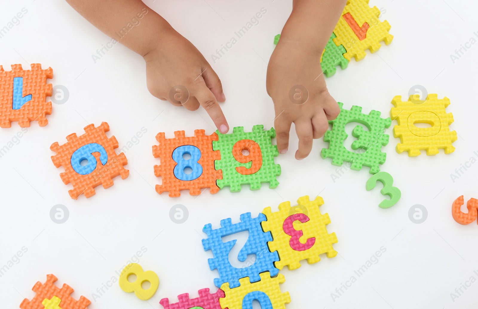 Photo of Little girl playing with colorful puzzles at white table, top view. Educational toy