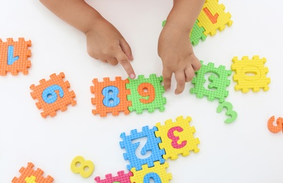 Little girl playing with colorful puzzles at white table, top view. Educational toy