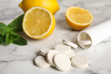 Bottle with vitamin pills and lemons on white marble table