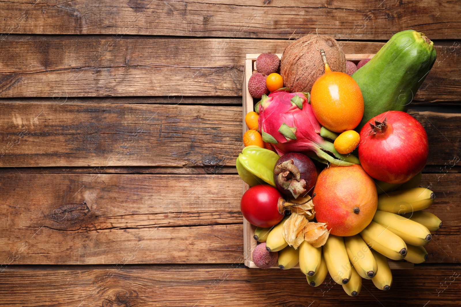 Photo of Crate with different exotic fruits on wooden table, top view. Space for text