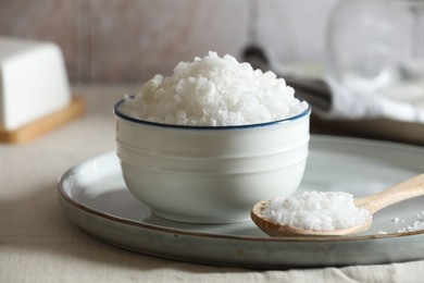 Photo of Organic salt in bowl and wooden spoon on table, closeup