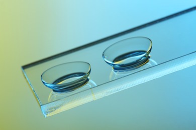 Photo of Pair of contact lenses on glass against color background, closeup