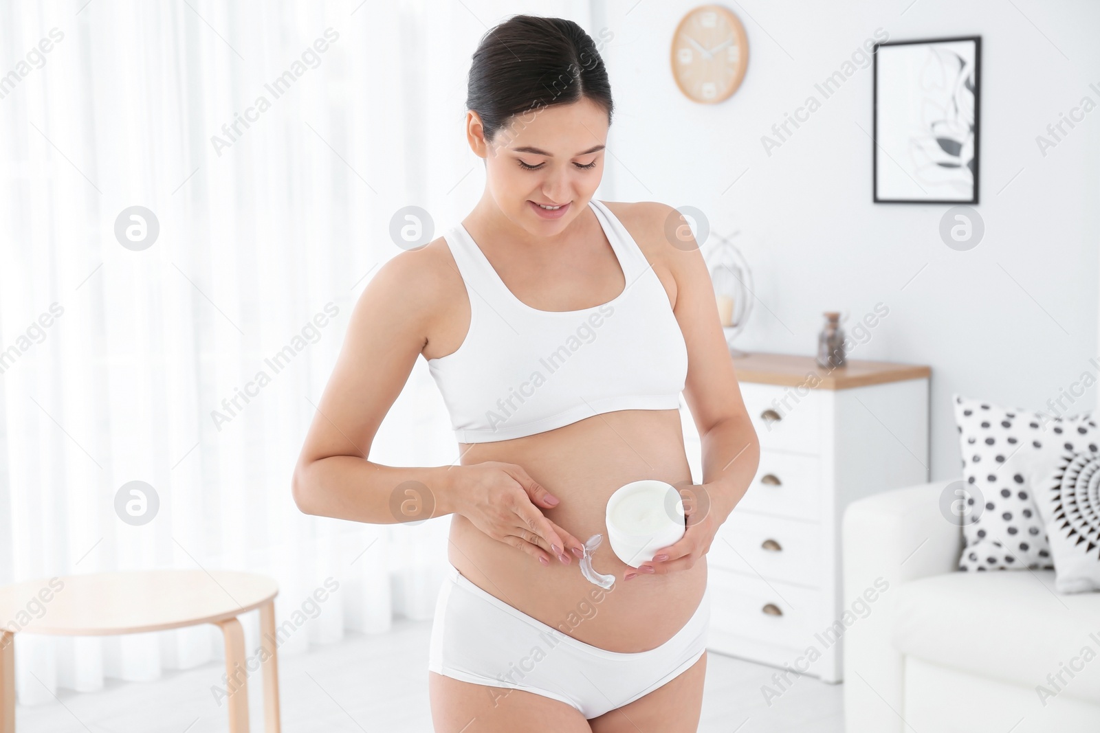 Photo of Pregnant woman applying body cream on belly at home