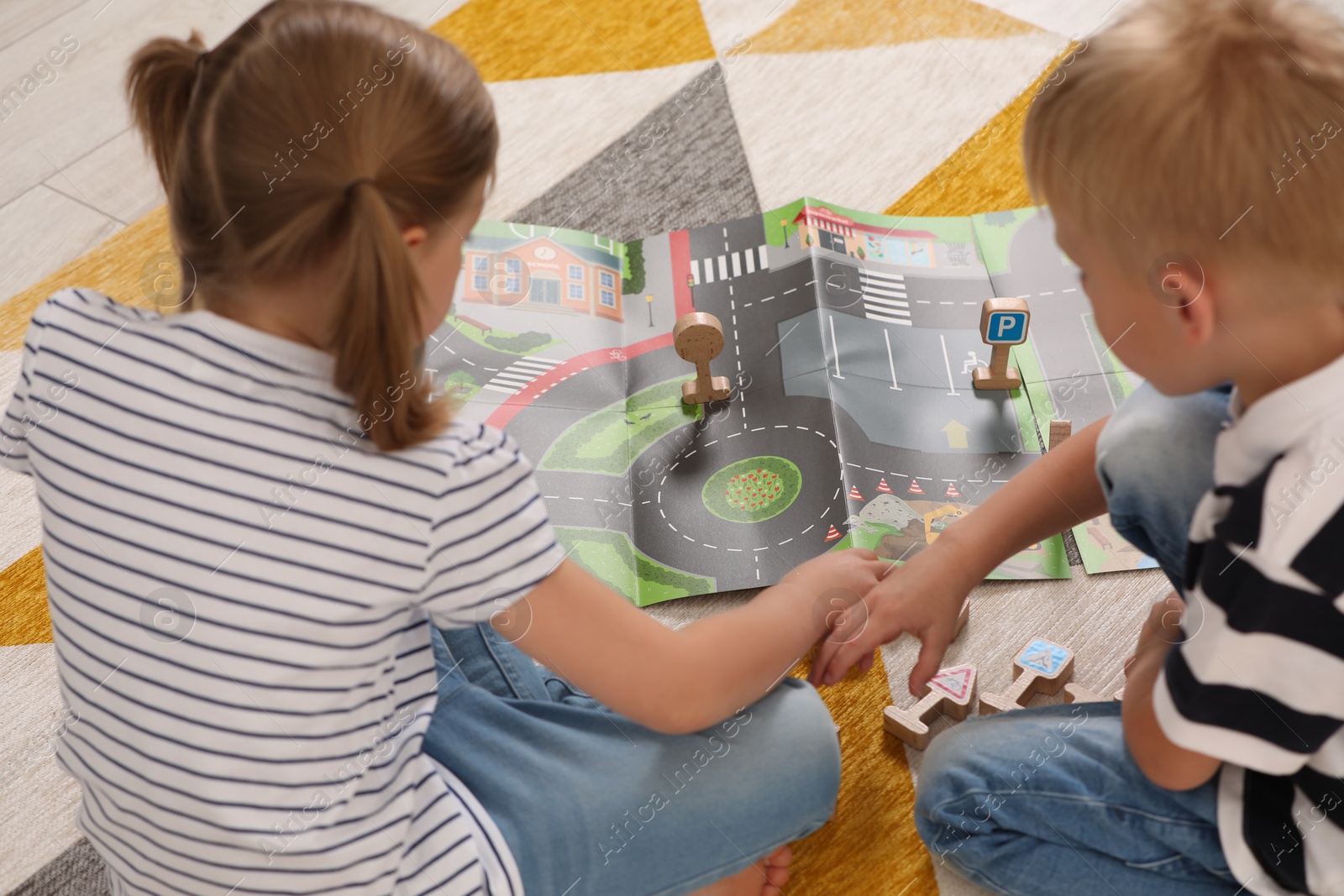 Photo of Little children playing with set of wooden road signs and toy cars indoors