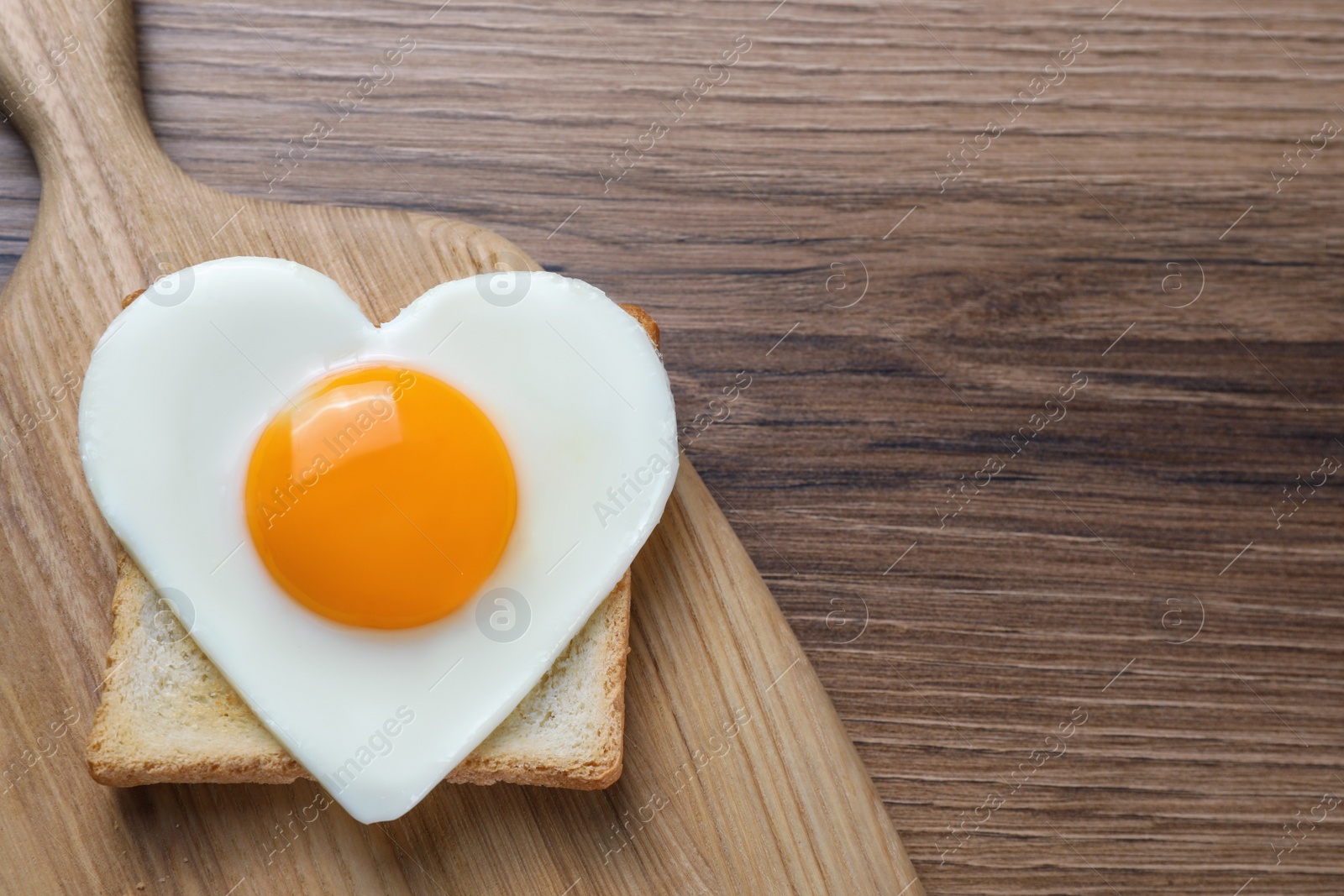 Photo of Heart shaped fried egg and toast on wooden table, top view. Space for text