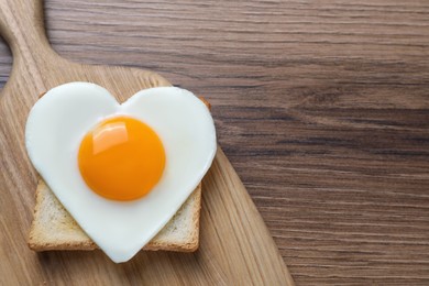 Photo of Heart shaped fried egg and toast on wooden table, top view. Space for text