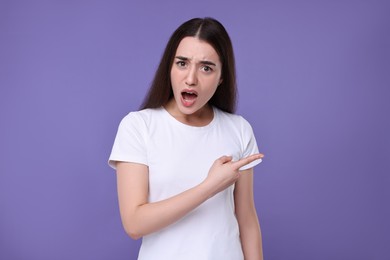 Photo of Portrait of surprised woman pointing at something on violet background