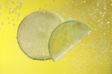 Photo of Juicy lime slices in soda water against yellow background, closeup