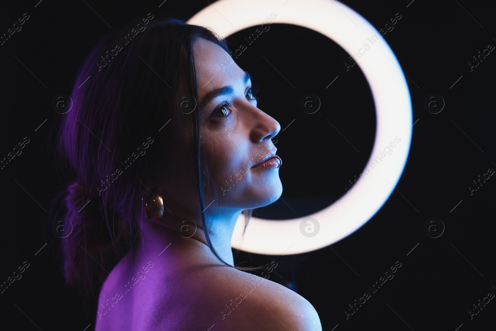 Photo of Beautiful woman and ring lamp on dark background in neon lights