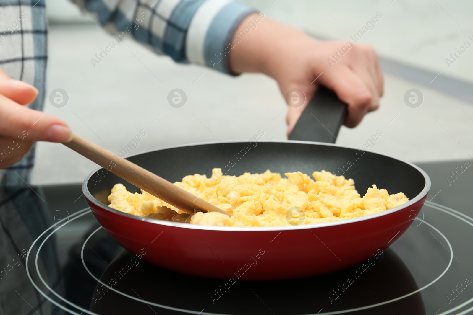 Photo of Woman cooking tasty scrambled eggs in frying pan on stove, closeup