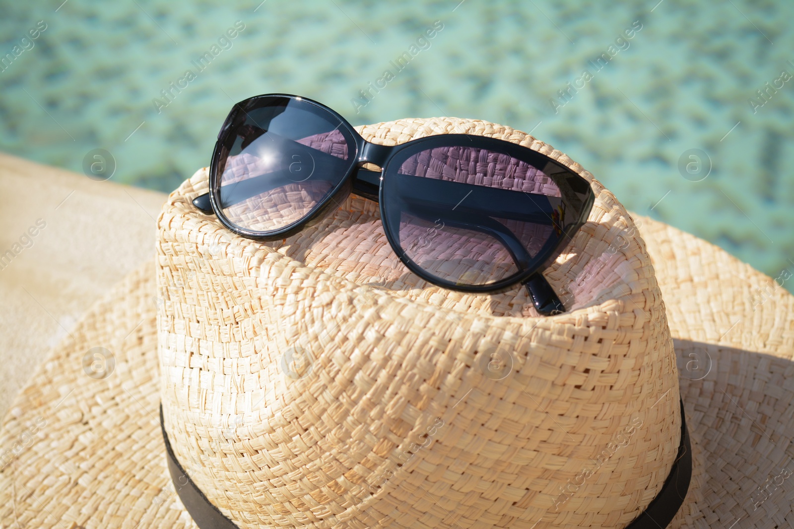 Photo of Stylish hat and sunglasses near outdoor swimming pool on sunny day, closeup