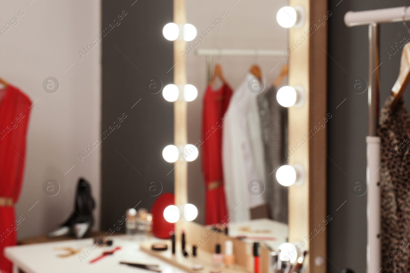 Photo of Blurred view of table with makeup products and mirror near grey wall in dressing room