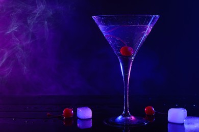 Photo of Fresh martini near ice and cherries on mirror table in neon lights, space for text