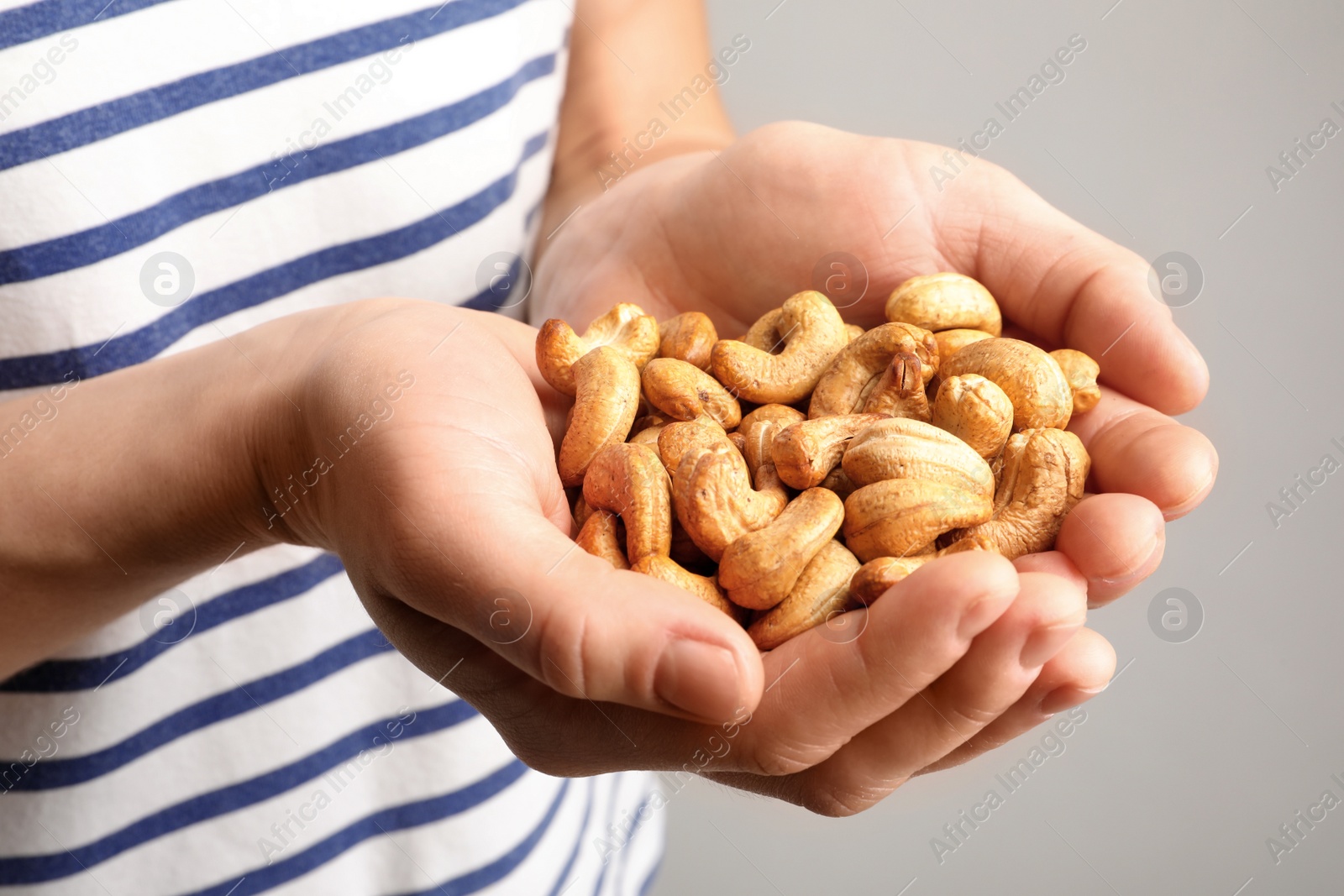 Photo of Woman holding cashew nuts on light background, closeup