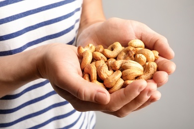 Woman holding cashew nuts on light background, closeup