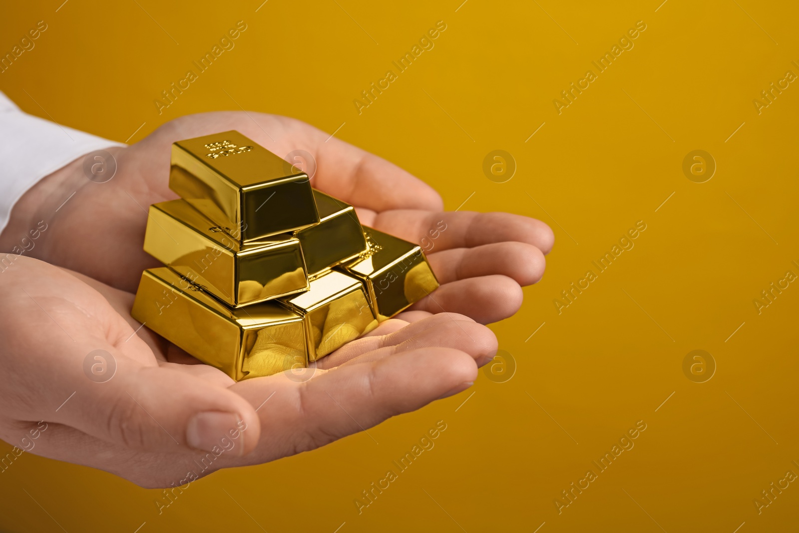 Photo of Woman holding many shiny gold bars on yellow background, closeup