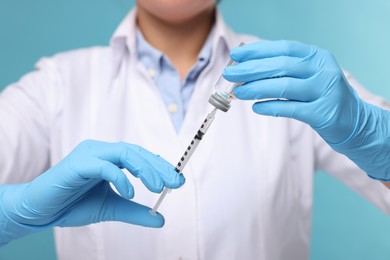 Photo of Doctor filling syringe with medication from glass vial on light blue background, closeup