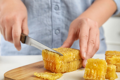 Photo of Woman cutting fresh honeycomb at table, closeup