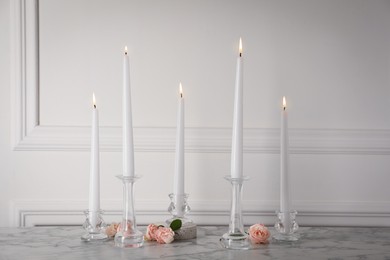 Photo of Elegant candlesticks with burning candles and flowers on white marble table